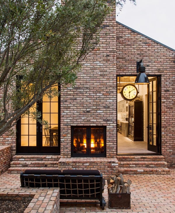 A red brick house with black window trim, and beautiful patio with a frieplace