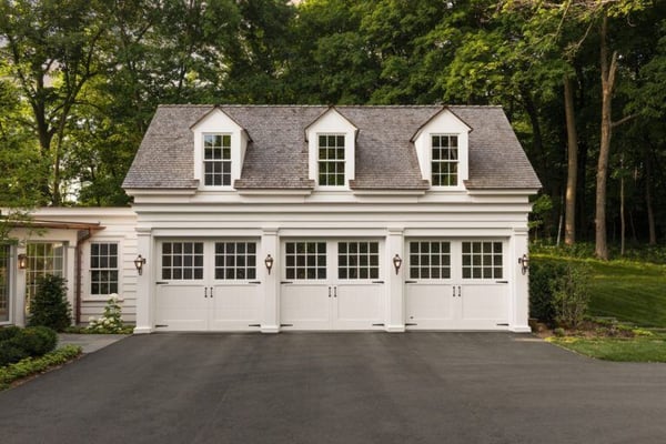 A white tradititional carriage house style garage with a connecting breezeway and garage doors with windows.