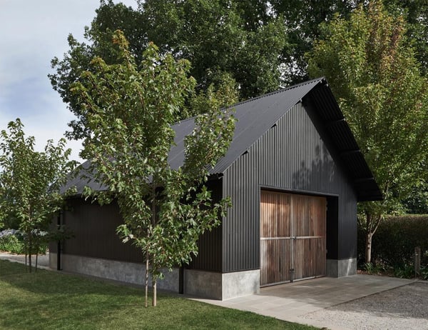 A barn-style detatched garage with a wooden garage door and black vertical siding.