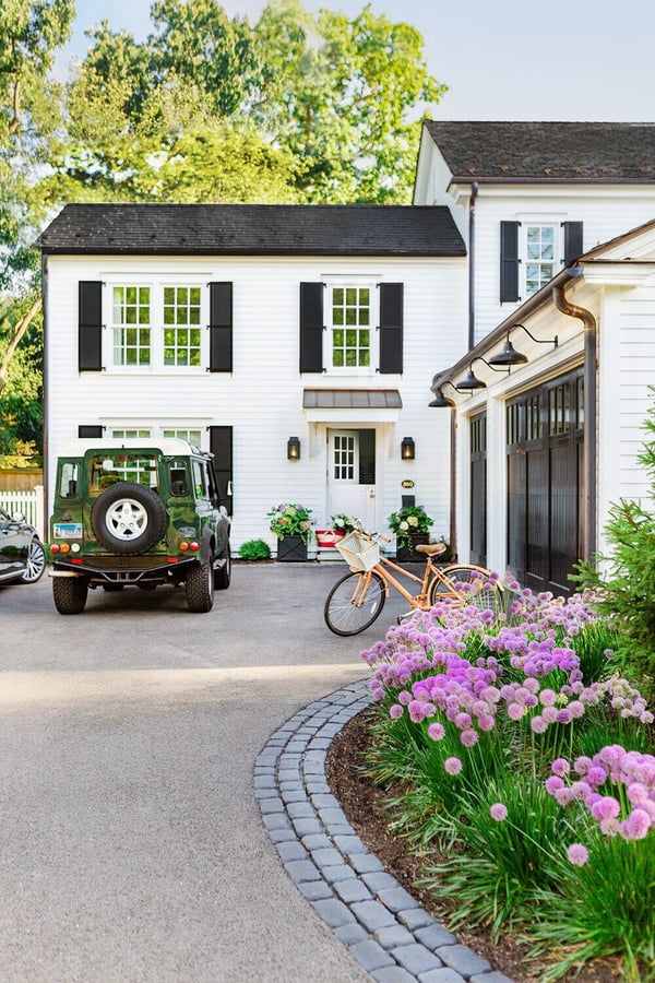 A New England style home with a garage with a black garage door with windows and exterior lighting sconces.
