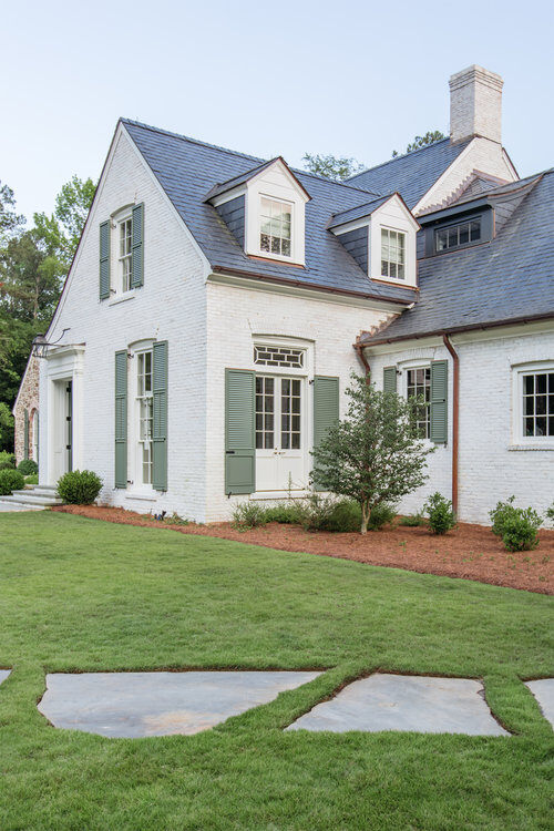 A limewash brick house with beautiful gutters, shutters and landscaping.