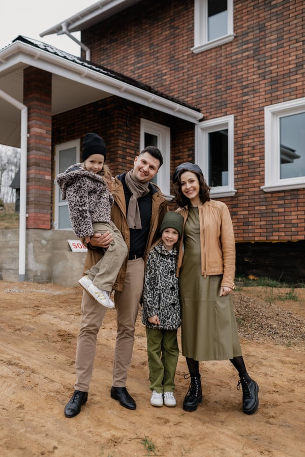 A family dressed warmly standing in front of a new red brick house.