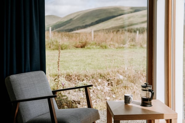 A mountain house living room with large window looking out to a green frield and mountain landscape