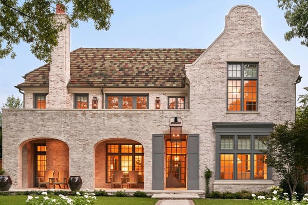 A beautiful brick house with a large ornate gable, long chimney, and large modern windows with a neatly landscaped front yard.