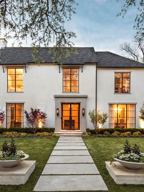 A cement pathway on a green landscaped lawn leading toward a gray stucco home with transitional windows 