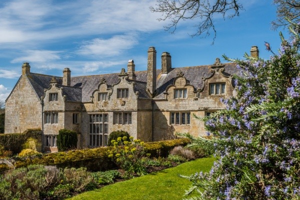 A historic English manor on a beautiful garden estate with a blue sky and wispy clouds in the background.