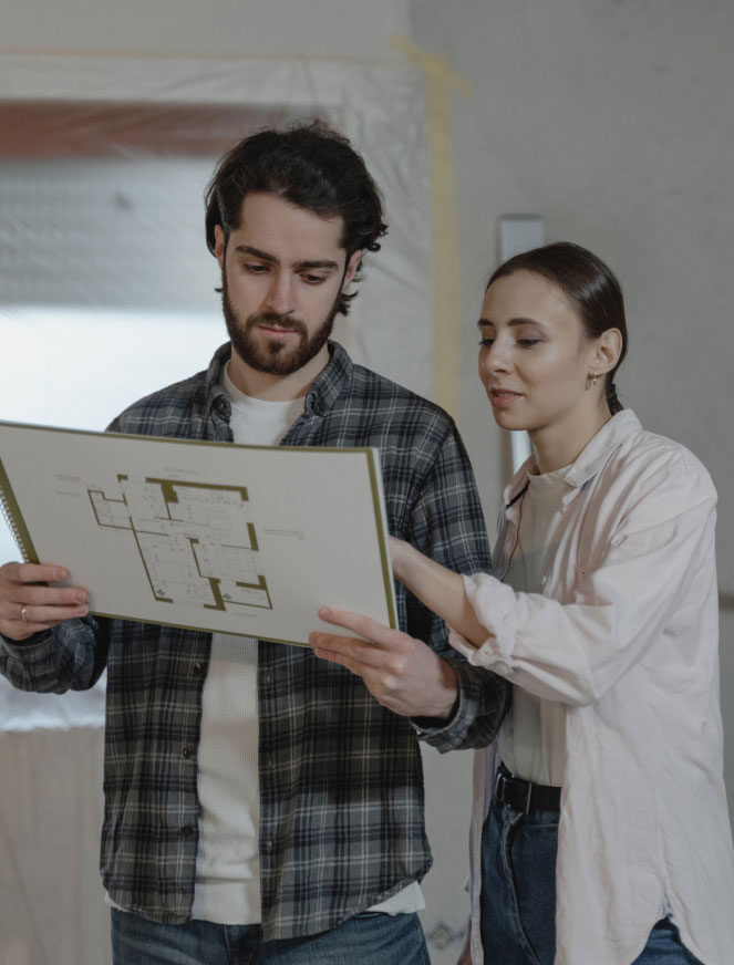 A man and woman look at construction documents together in an unfinished buildling A man and woman look at construction documents together in an unfinished buildling